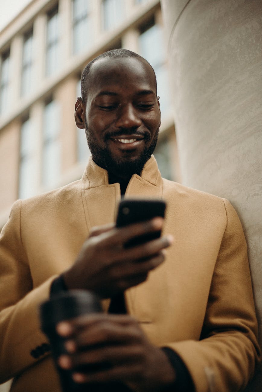 smiling man looking at his phone leaning on concrete pillar